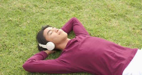 Young Man Relaxing on Park Grass Wearing White Headphones