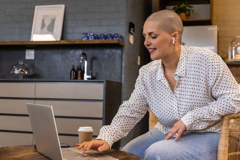 Remote working woman with shaved head typing on laptop at cozy modern kitchen table