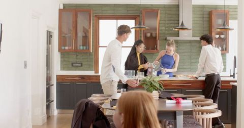 Friends gathering at modern kitchen island pouring drinks and sharing food