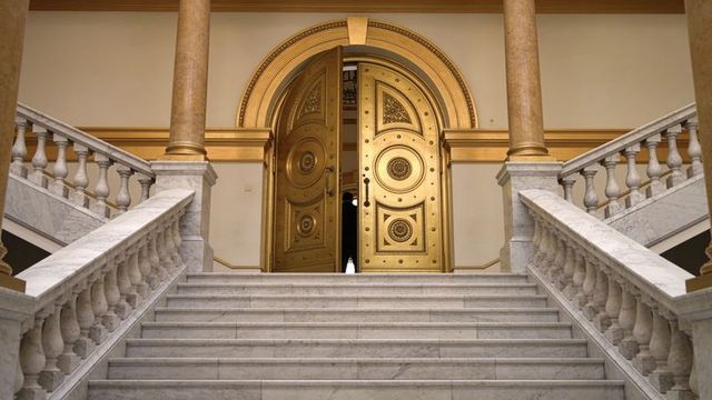 Silhouette entering grand gilded doors at marble staircase, neoclassical opulent interior