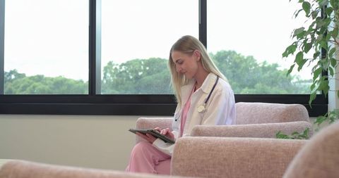 Female clinician reviewing patient records on tablet in sunlit clinic waiting room