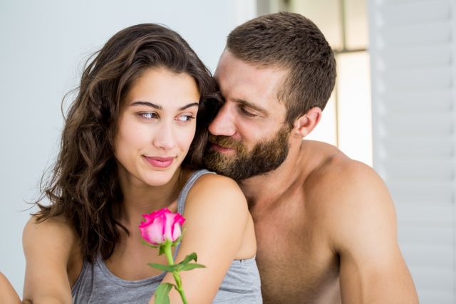 Man offering a rose to a woman at home, both smiling and sharing an intimate moment. Ideal for use in romantic, relationship, and Valentine's Day themes, as well as advertisements for gifts, flowers, and home decor.