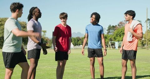 Male athletes standing on sunny sports field sharing conversation and camaraderie