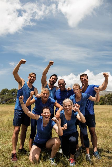 Group of fit individuals celebrating success in an outdoor boot camp on a sunny day. They are wearing sportswear and showing team spirit and unity. Ideal for use in fitness, teamwork, and healthy lifestyle promotions, as well as motivational and sports-related content.