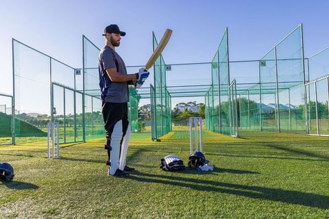 Cricketer preparing at outdoor practice nets with bat and protective gear