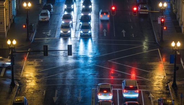 Wet urban intersection at night with glowing headlights and vibrant streetlight reflections