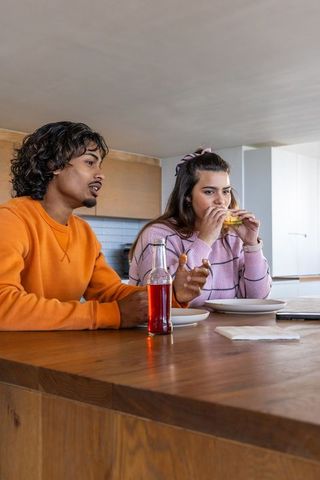 Young couple eating and talking at wooden kitchen island, casual contemporary home dining