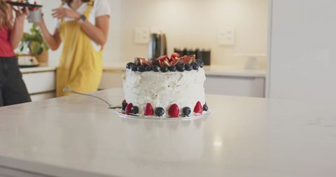 Women chatting while serving frosted berry cake on modern minimalist kitchen island