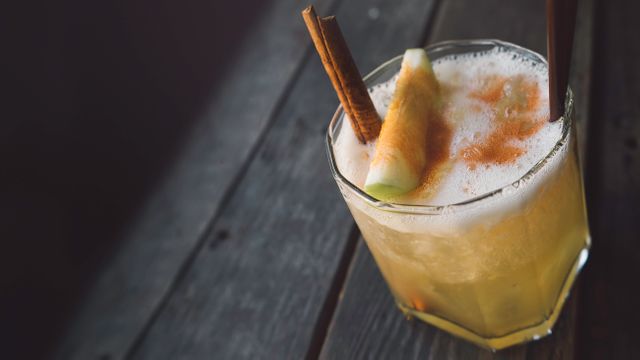 A delicious, refreshing cocktail served in a glass with a foamy top, garnished with a cinnamon stick and a slice of apple. Ideal for illustrating articles on drinks, recipes for summer cocktails, and ingredients for creating unique beverages. Can be used in menus, food and drink blogs, or social media posts for bars and restaurants.
