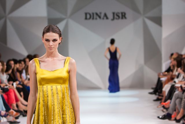 Fashion model wearing a striking yellow dress walking down runway, capturing elegance and sophistication of designer's collection. Perfect for use in fashion magazines, blogs, social media posts, advertisements, and articles highlighting runway events, designer showcases, and contemporary fashion trends.