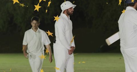 Cricket player standing in white kit wearing bucket hat at night on grass with golden stars overlay