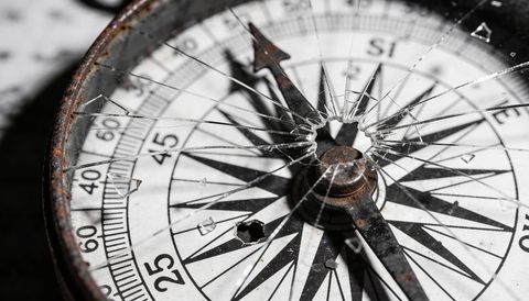 Shattered glass on rusted antique compass featuring corroded needle and weathered dial