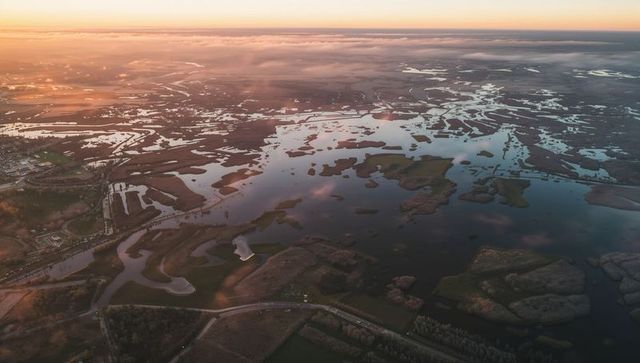 Capturing aerial estuary sunset with winding tidal channels, reflective waters and rural causeway