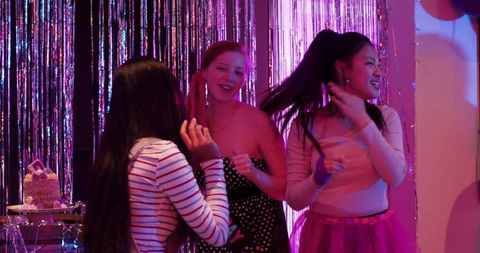 Diverse women dancing at magenta party with metallic fringe curtain and celebration cake