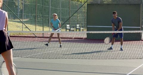 Tennis doubles partners playing at net on sunlit outdoor hard court