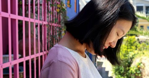 Contemplative Young Woman Enjoying Outdoor Serenity by Pink Fence