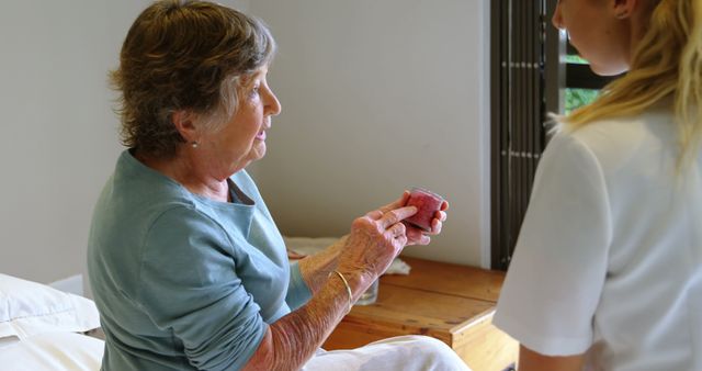 Senior woman sitting on hospital bed receiving medical assistance from healthcare professional, highlighting elderly care and support. Ideal for use in articles about healthcare services, elderly well-being, and medical support.