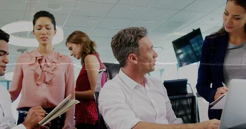Mature leader guiding collaborative team meeting in bright open-plan office with laptop