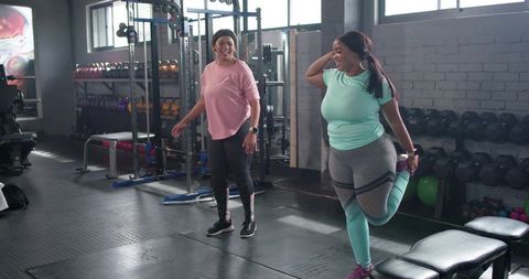 Diverse mid-adult black women stretching together in gym wearing colorful activewear