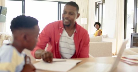 African american father helping son with homework while mother smiling in living room