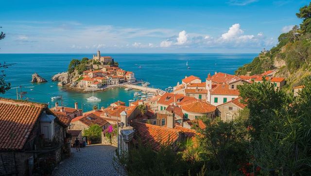 Sunlit mediterranean harbor with terracotta roofs and church islet overlooking azure sea