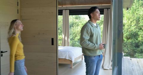 Couple enjoying morning in modern cabin bedroom by sliding glass door and deck