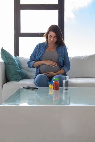 Pregnant Woman Relaxing at Home with Medication and Water on Table