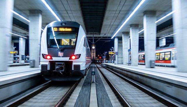 Night commuter train arriving at modern station with illuminated canopy and clock tower