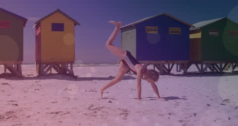 Girl Practicing Handstands on Sunny Beach with Colorful Beach Huts