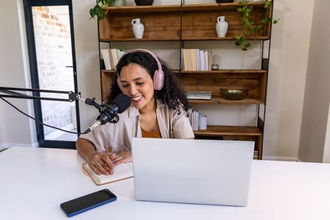 African american woman podcasting, taking notes in home studio with laptop and microphone