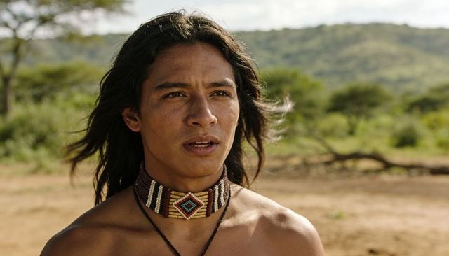 Standing gazing bare-chested man wearing beaded choker on sunlit savanna landscape