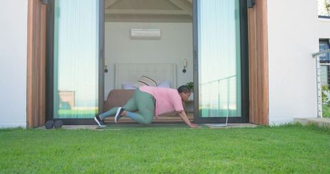 Midlife african american woman exercising at home doorway with laptop and dumbbells