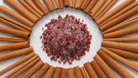 Whole cinnamon sticks forming radial ring around pile of red rock sugar crystals on white