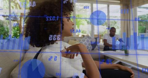 Woman leaning on sofa while partner working on laptop with blue data visualization overlay