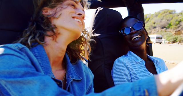 Two friends smiling and laughing while driving a convertible on a sunny day. They are enjoying freedom and adventure, highlighted by the bright and cheerful atmosphere. This image can be used to depict joyful moments, road trip adventures, friendship, and summer vibes.