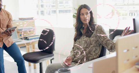 Woman gesturing while discussing project with colleague in bright modern office