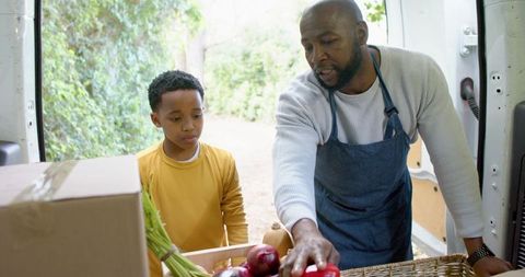 African american farmer delivering fresh produce from farm van while teaching young boy