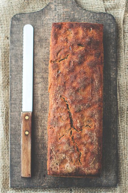 Freshly baked rye bread placed on a rustic wooden cutting board with a knife next to it. Ideal for use in food blogs, bakery promotions, cooking videos, recipe books, healthy eating articles, and culinary websites displaying artisanal bread and homemade baking. The earthy tones and simple background evoke a warm, wholesome feeling, perfect for promoting natural and organic food.