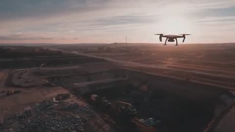 Sunset drone surveying open-pit quarry, hovering over stockpiles and heavy machinery