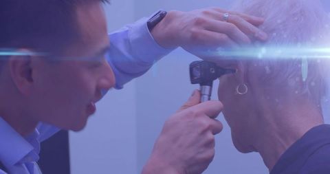 Doctor Examining Elderly Patient's Ear with Otoscope and Blue Light Effects