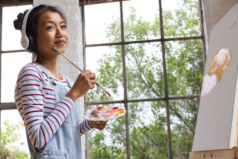 Asian woman in art studio painting by sunlit window