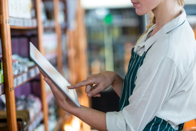Female staff member using a digital tablet in a supermarket. Ideal for illustrating modern retail technology, inventory management, and efficient customer service in grocery stores. Useful for business presentations, retail technology articles, and marketing materials for retail solutions.