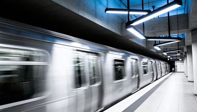 Rushing silver commuter train streaming through modern concrete metro platform at night