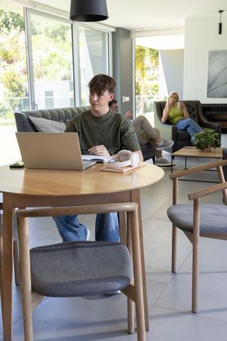 African family modern living-dining, teen studying on laptop at round wooden table