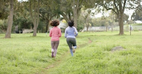 Two women running on meadow trail, outdoor fitness, friendship, active lifestyle
