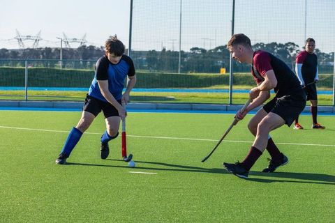 Competitive male athletes playing field hockey on artificial turf