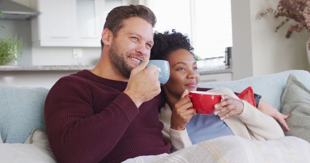Image of happy diverse couple embracing and drinking coffee on sofa. Love, relationship and spending quality time together at home.