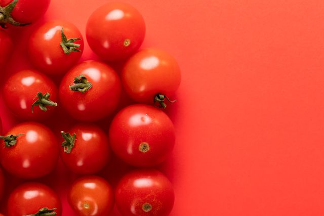 Fresh cherry tomatoes arranged on a red background, creating a vibrant and colorful scene. Ideal for use in healthy eating promotions, organic food advertisements, vegetarian and vegan diet materials, and nutritional guides. The bright red background enhances the freshness and appeal of the tomatoes, making it perfect for food blogs, recipe websites, and culinary magazines.