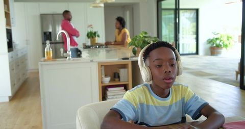 African american family talking in modern kitchen, child wearing headphones at table