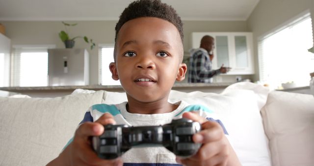 Young boy focusing intensely on playing a video game, holding a game controller at home. Perfect for topics related to childhood entertainment, leisure activities, video game usage, and tech-savvy kids. Useful in parent blogs, gaming websites, or lifestyle publications emphasizing youth hobbies.